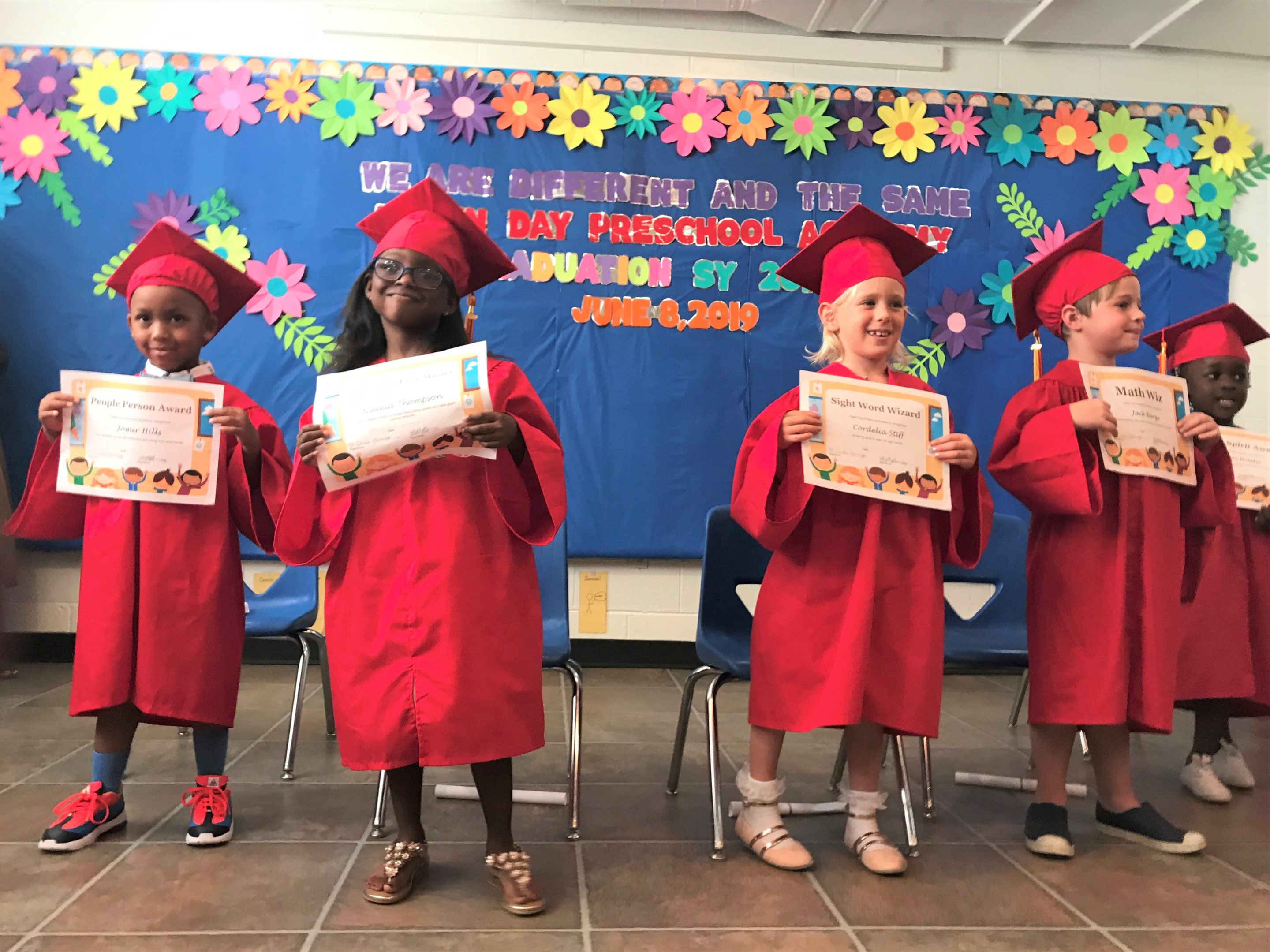 Four Hopkins House students celebrate their graduation, holding diplomas in their caps and gowns
